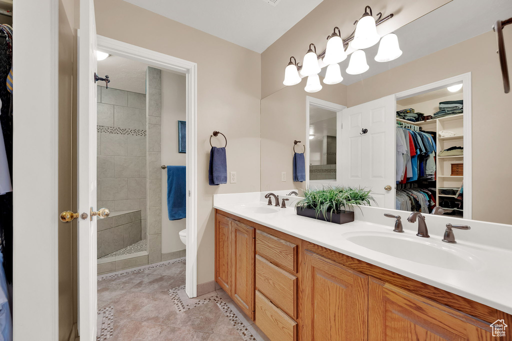 Full bath featuring double vanity, a walk in closet, tiled shower, and tile patterned flooring