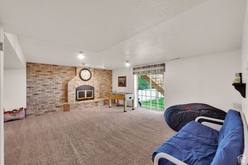Living area with carpet flooring, a fireplace, brick wall, and a textured ceiling