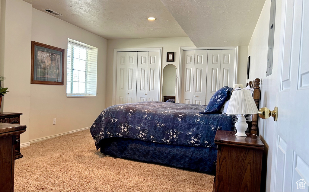 Carpeted bedroom featuring multiple closets, a textured ceiling, and recessed lighting