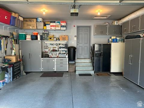 Garage with black fridge, a workshop area, and a garage door opener