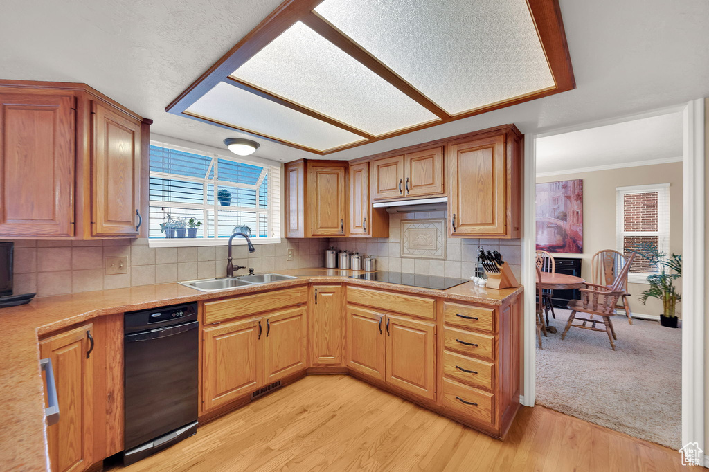 Kitchen with light countertops, decorative backsplash, light wood-style flooring, ornamental molding, and black electric stovetop