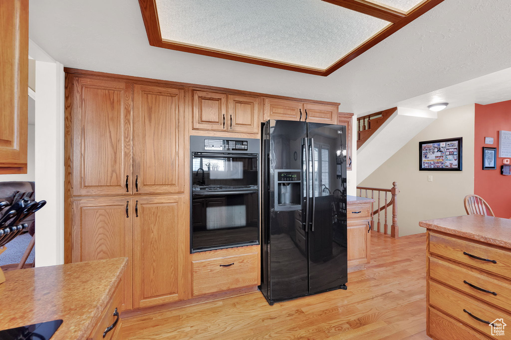 Kitchen with black appliances, light wood finished floors, and light countertops