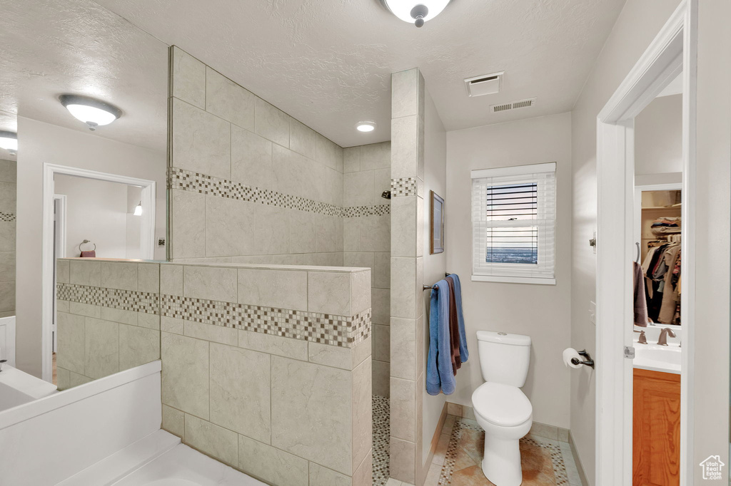 Full bathroom with a walk in shower, vanity, a walk in closet, tile patterned flooring, and a textured ceiling