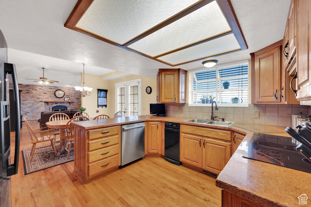 Kitchen featuring black appliances, a peninsula, ceiling fan, decorative backsplash, and light wood-type flooring