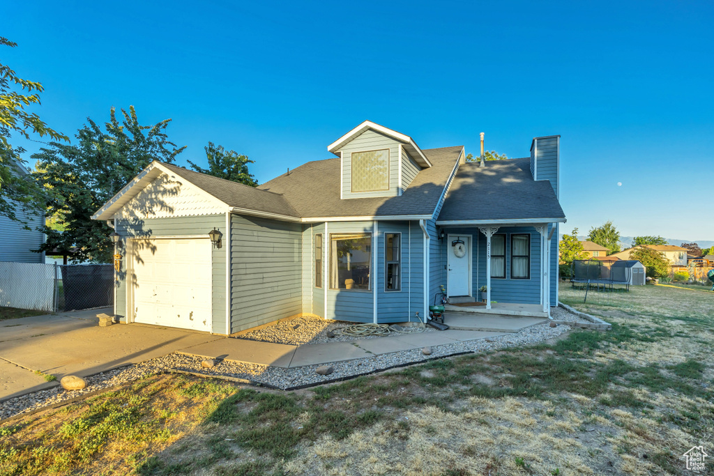 View of front of house featuring an attached garage, a chimney, driveway, a shingled roof, and a storage unit
