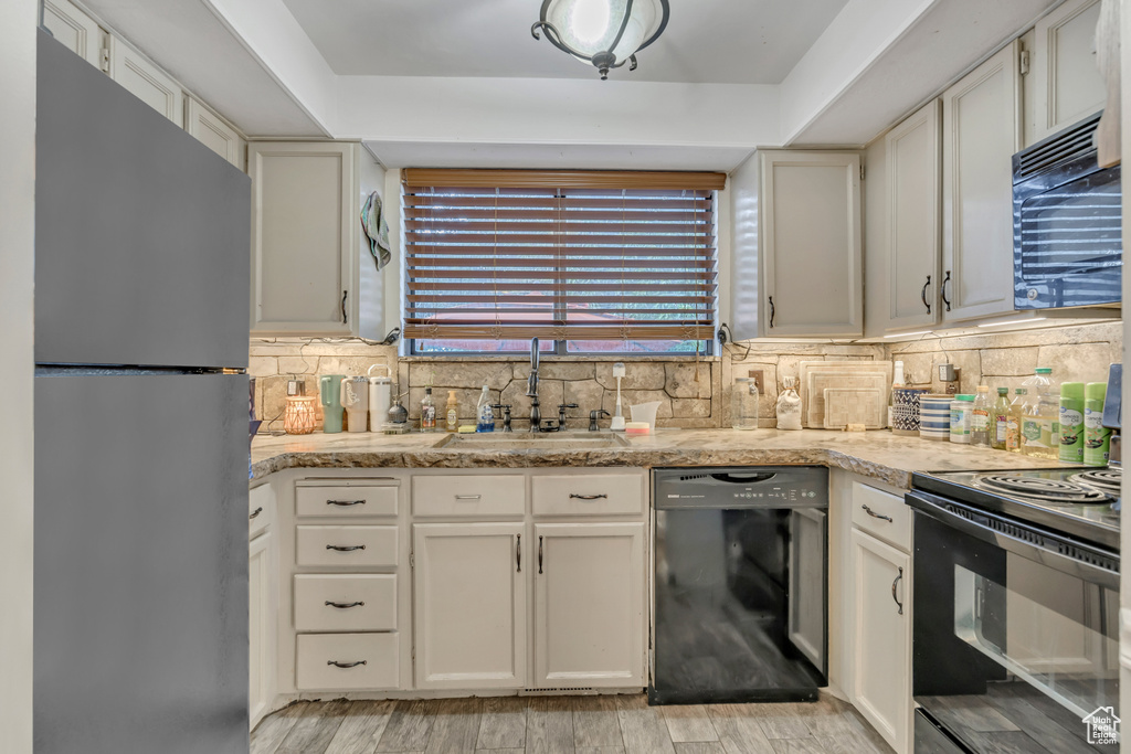Kitchen featuring black appliances, decorative backsplash, light wood-type flooring, and white cabinetry