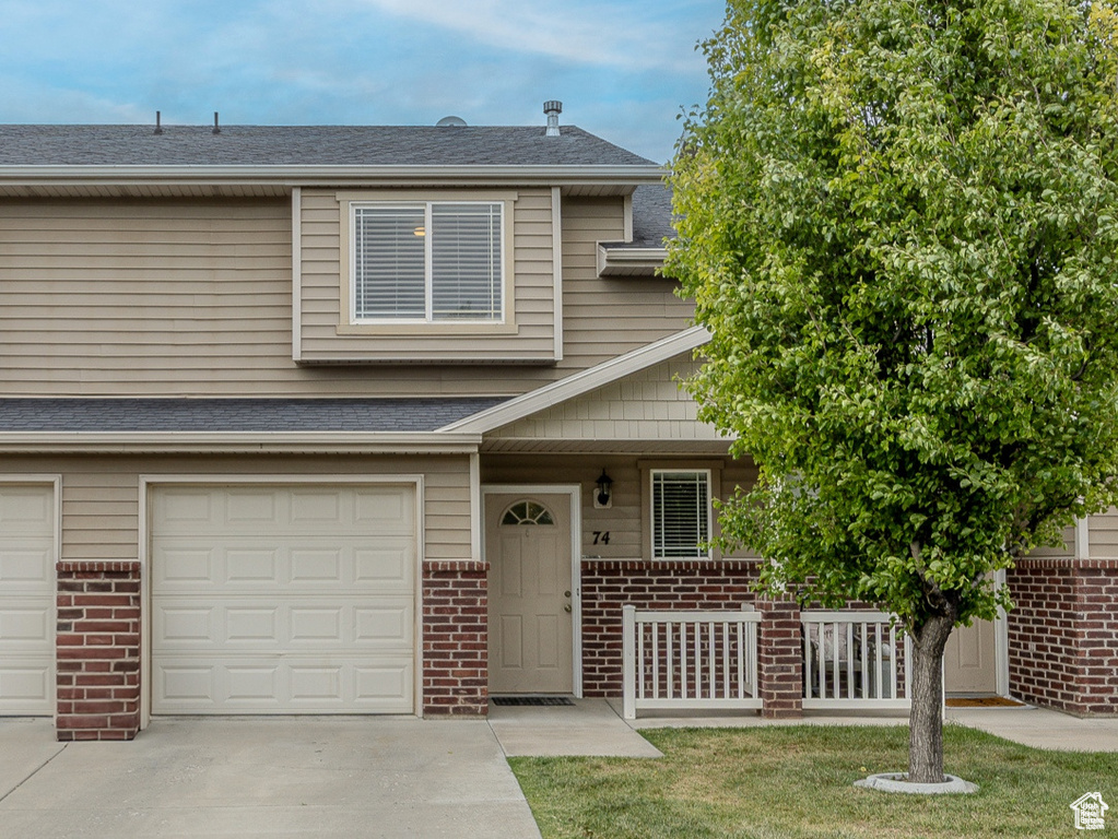 Multi unit property featuring brick siding, covered porch, driveway, an attached garage, and a shingled roof