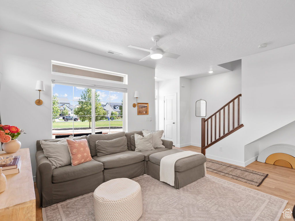 Living room featuring wood finished floors, a ceiling fan, stairs, and a textured ceiling