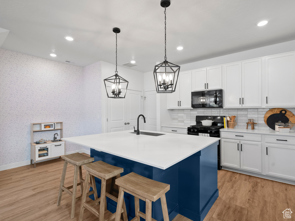 Kitchen with black appliances, light wood finished floors, a chandelier, decorative backsplash, and recessed lighting