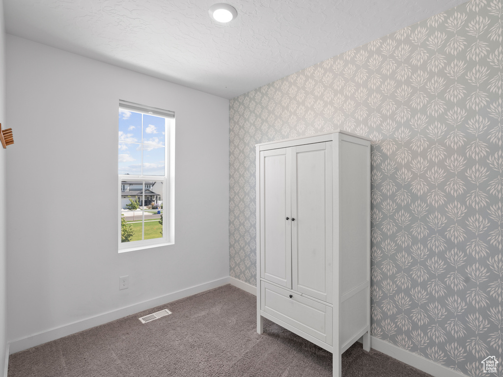 Unfurnished bedroom with wallpapered walls, carpet floors, and a textured ceiling