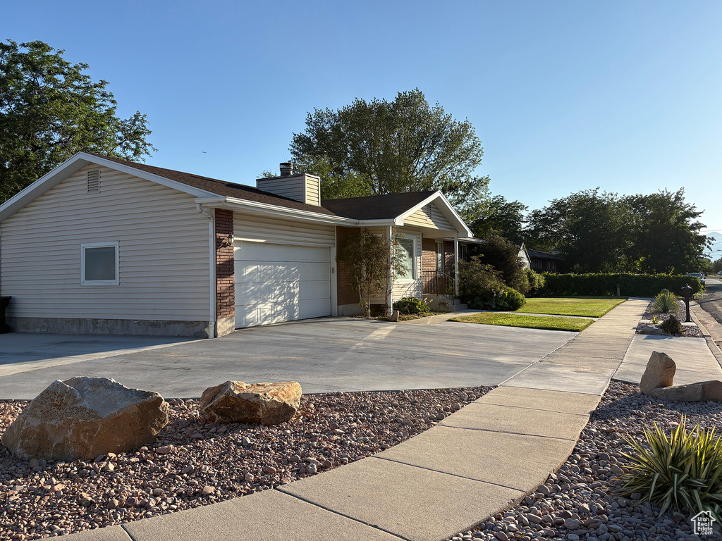 View of side of home with a chimney, an attached garage, driveway, and brick siding