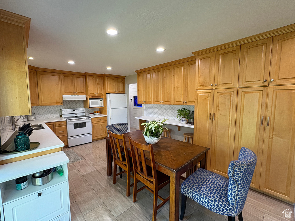 Kitchen with white appliances, under cabinet range hood, decorative backsplash, light countertops, and recessed lighting