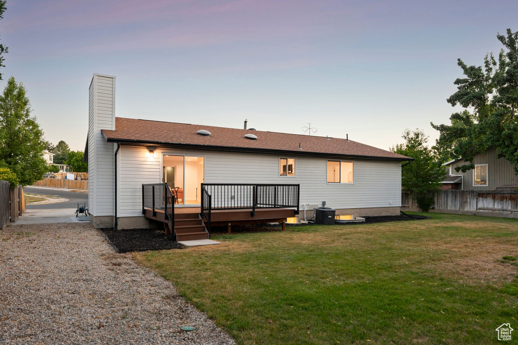 Back of house at dusk featuring a fenced backyard, a deck, and a chimney