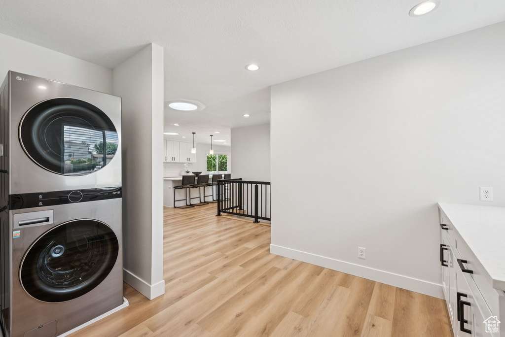 Laundry room with stacked washer and clothes dryer, light wood finished floors, and recessed lighting