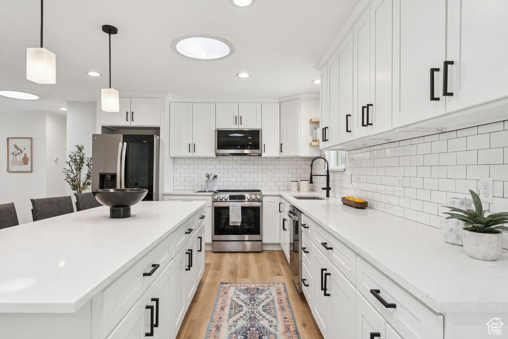 Kitchen with appliances with stainless steel finishes, light wood-style floors, a center island, white cabinetry, and recessed lighting