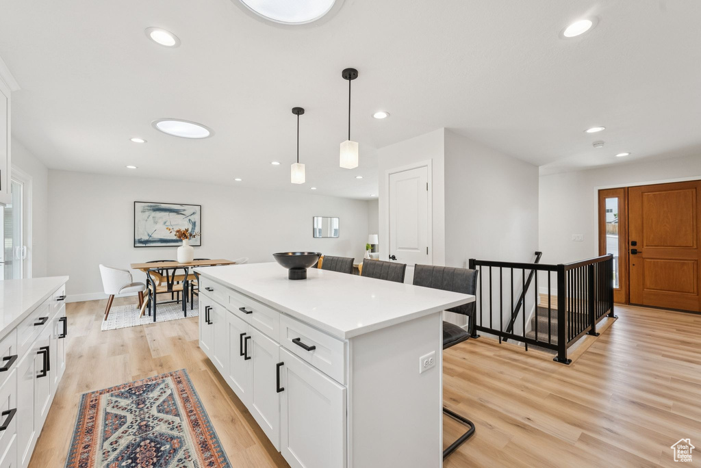 Kitchen with a breakfast bar area, a center island, light wood-style flooring, pendant lighting, and white cabinets