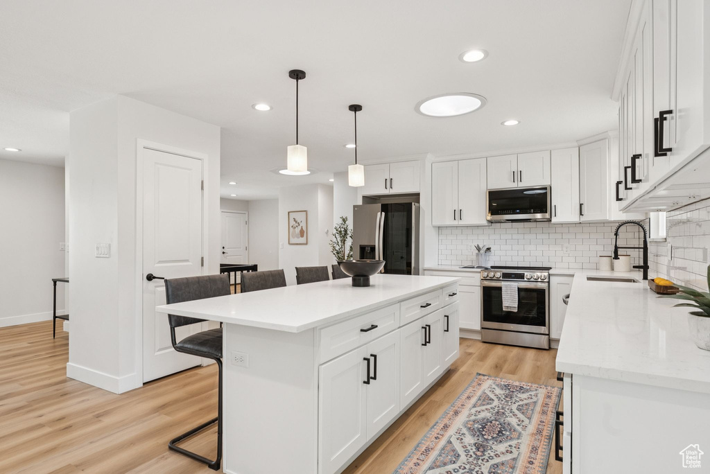 Kitchen with stainless steel appliances, a kitchen breakfast bar, decorative backsplash, light wood finished floors, and white cabinetry