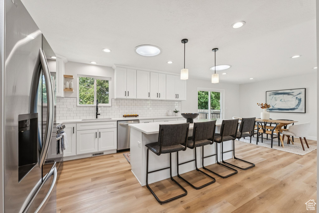 Kitchen featuring stainless steel appliances, light countertops, backsplash, light wood-style flooring, and white cabinets
