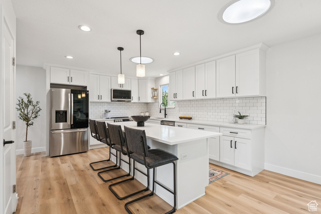 Kitchen with stainless steel appliances, light wood-style flooring, decorative backsplash, white cabinetry, and recessed lighting