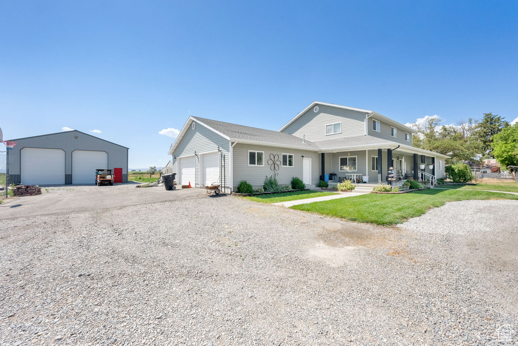 View of front facade featuring covered porch, a front lawn, a detached garage, and gravel driveway