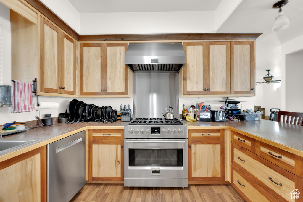 Kitchen with appliances with stainless steel finishes, wall chimney range hood, light brown cabinetry, and light wood-type flooring