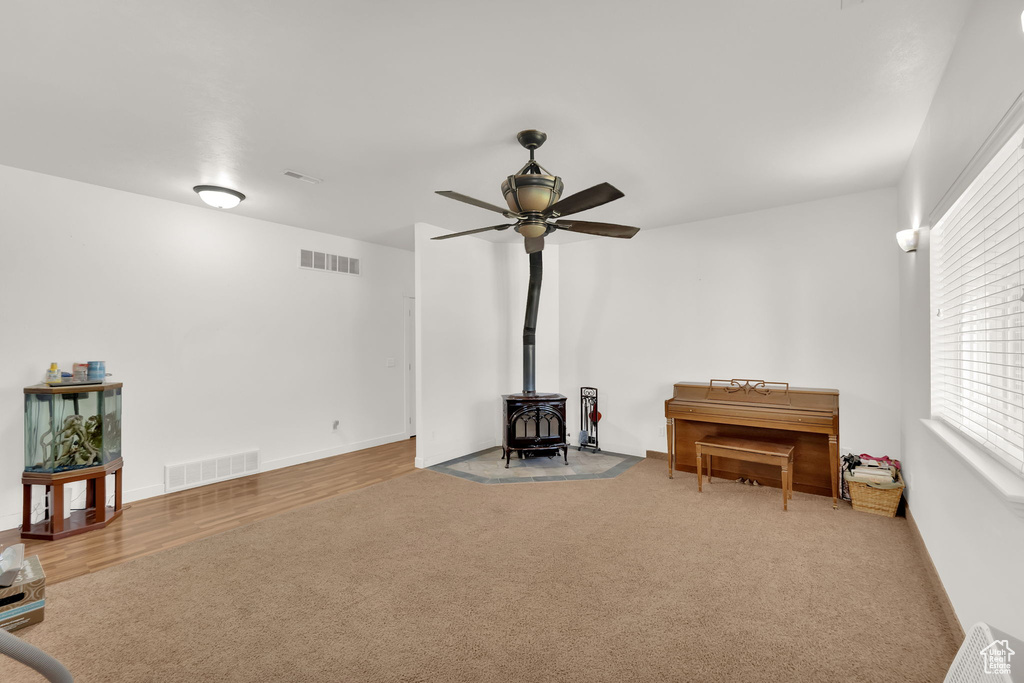 Sitting room featuring a wood stove, carpet floors, and ceiling fan
