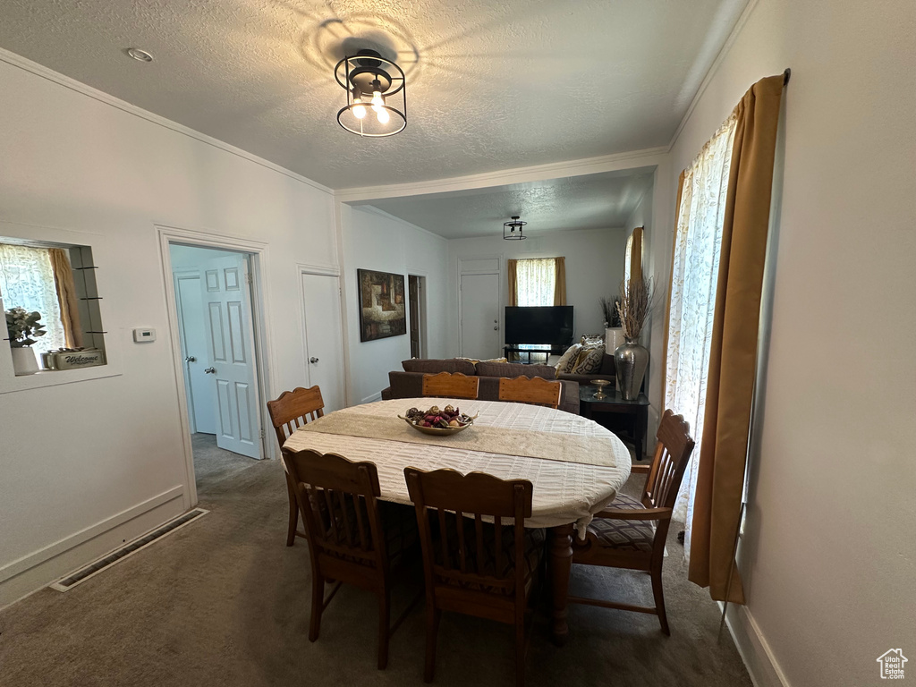 Dining room with dark colored carpet, ornamental molding, and a textured ceiling