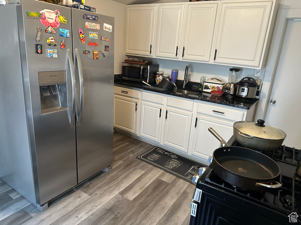 Kitchen with stainless steel appliances, light wood-type flooring, white cabinetry, and dark stone counters