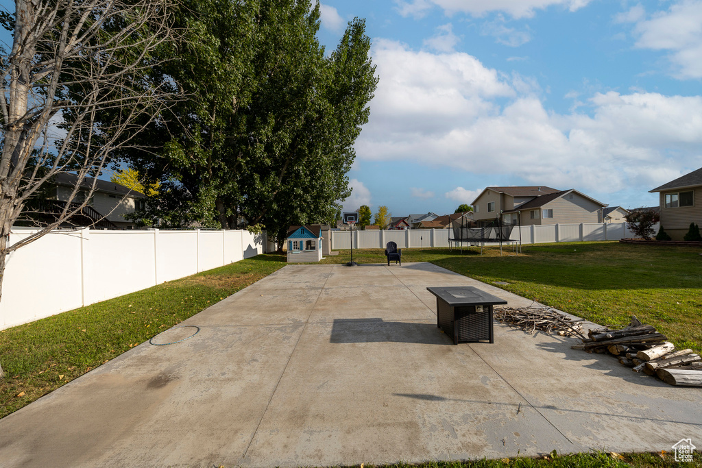 Fenced backyard with a trampoline, a patio area, a residential view, and a shed