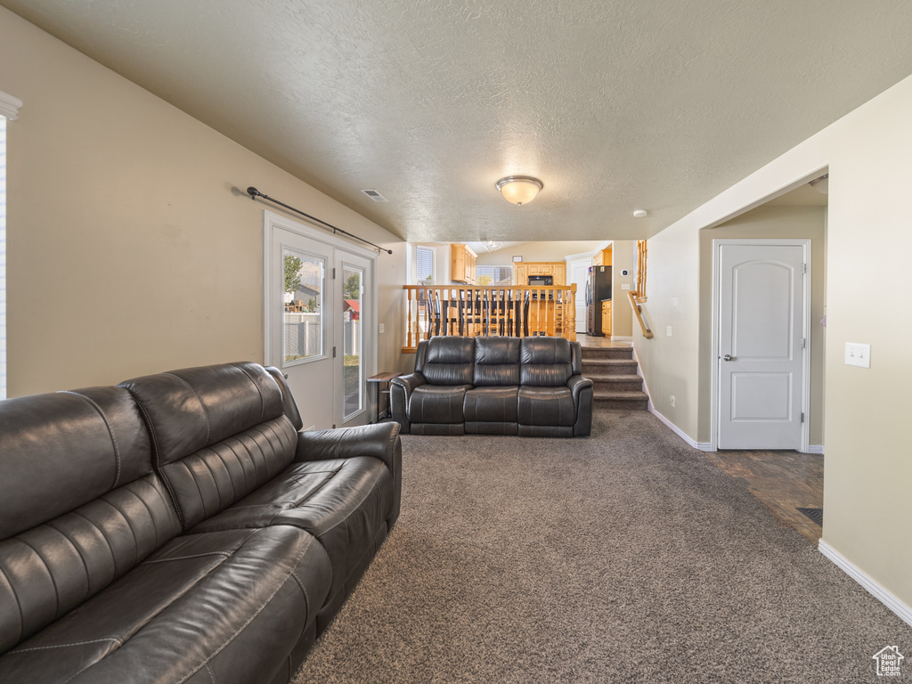 Living room featuring dark colored carpet, stairs, and a textured ceiling