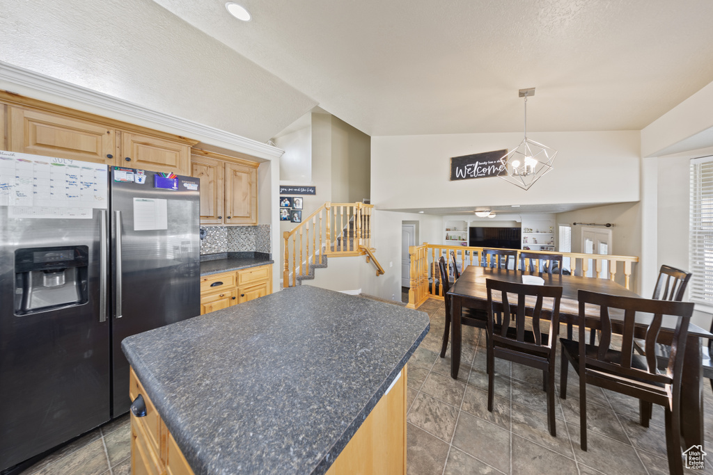 Kitchen with stainless steel fridge, dark countertops, light brown cabinets, a chandelier, and tasteful backsplash