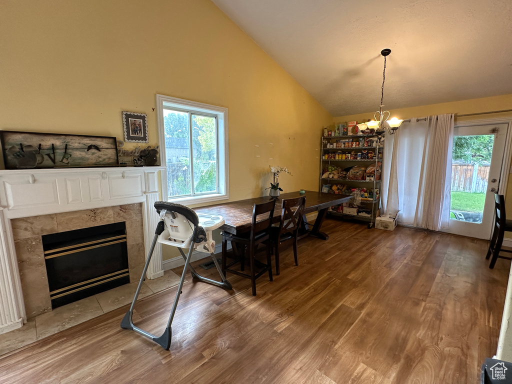 Dining area with a chandelier, wood finished floors, lofted ceiling, and a tiled fireplace