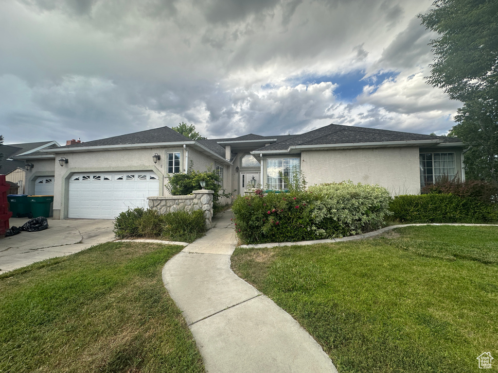 Ranch-style home featuring an attached garage, a front yard, driveway, and stucco siding