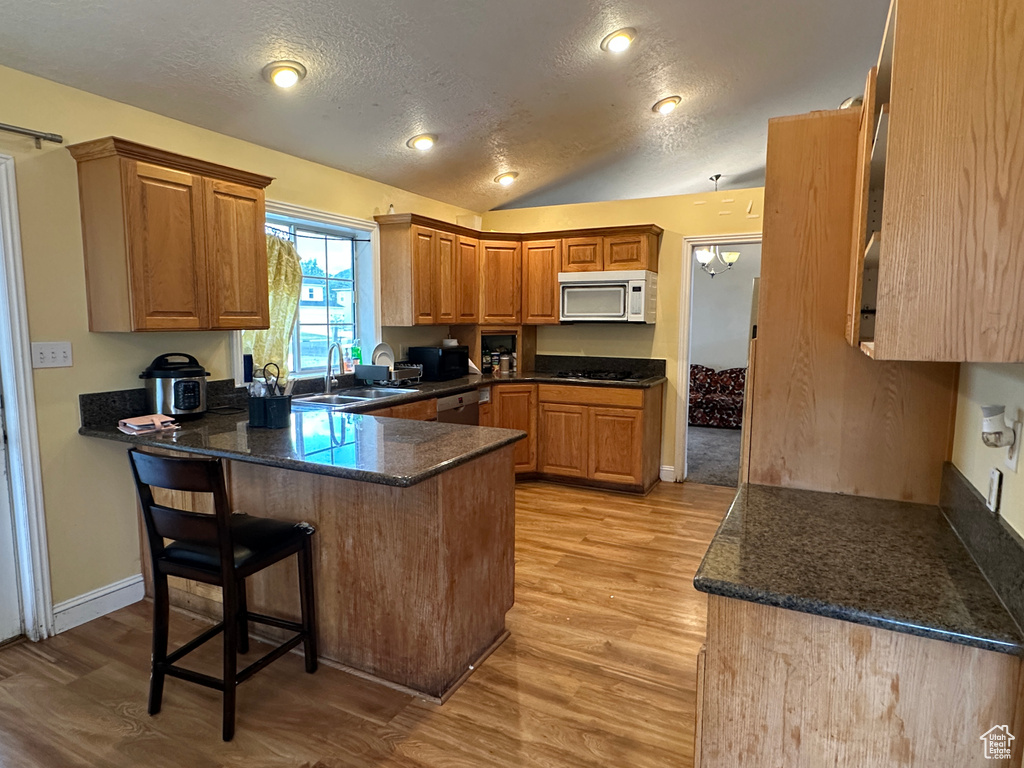 Kitchen featuring white microwave, a peninsula, light wood finished floors, a textured ceiling, and a breakfast bar