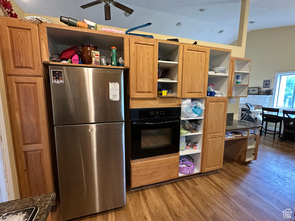 Kitchen with freestanding refrigerator, open shelves, black oven, light wood-style floors, and ceiling fan