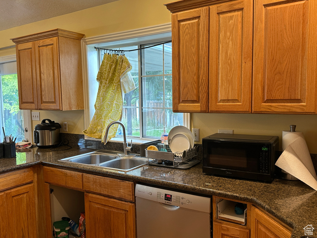 Kitchen featuring dishwasher, black microwave, brown cabinets, and dark stone countertops