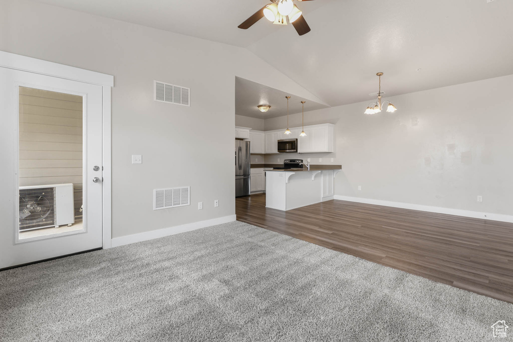 Unfurnished living room featuring vaulted ceiling, a ceiling fan, dark colored carpet, and a chandelier