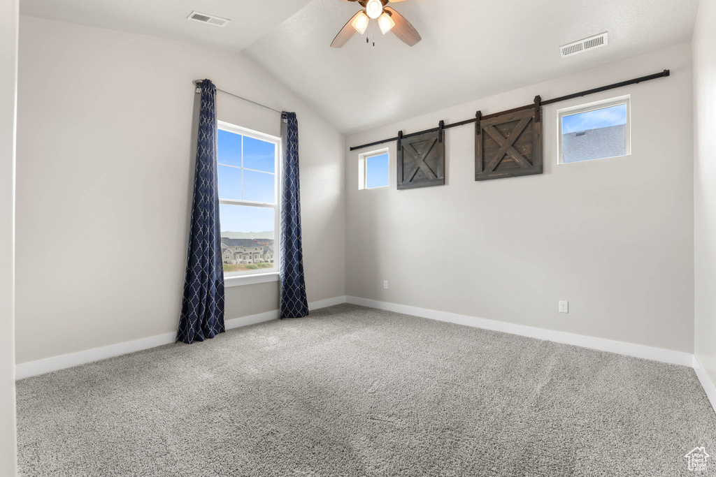 Spare room with ceiling fan, carpet flooring, vaulted ceiling, and a barn door
