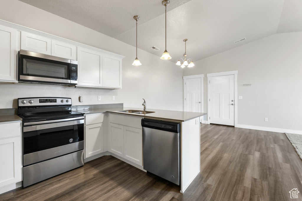 Kitchen with appliances with stainless steel finishes, lofted ceiling, dark wood finished floors, white cabinets, and a chandelier