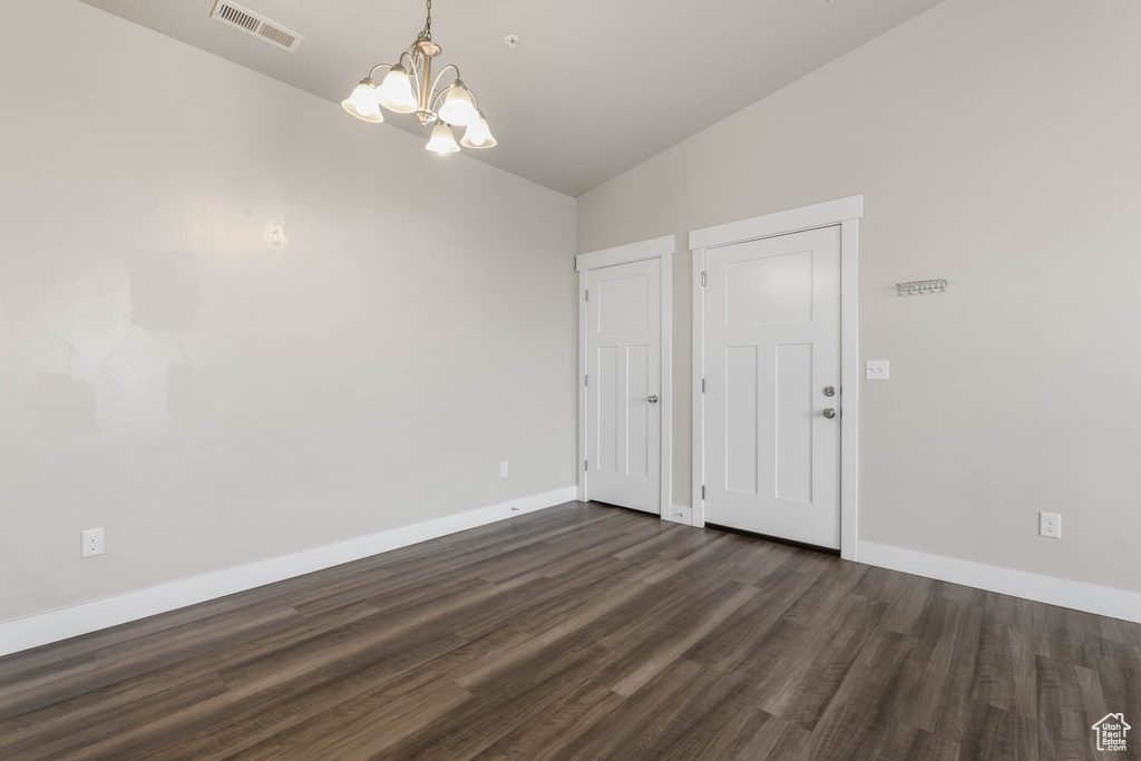 Unfurnished dining area with lofted ceiling, a chandelier, and dark wood-type flooring