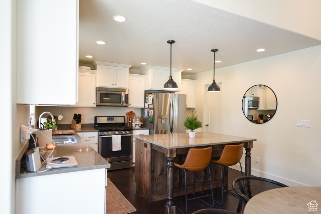 Kitchen with appliances with stainless steel finishes, recessed lighting, white cabinets, a kitchen breakfast bar, and a kitchen island