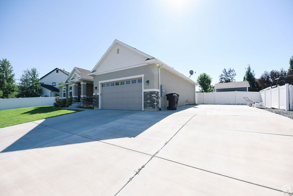 View of side of home featuring an attached garage, driveway, stone siding, and stucco siding