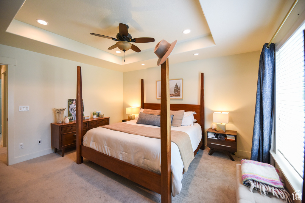 Bedroom with a tray ceiling, light colored carpet, recessed lighting, and ceiling fan