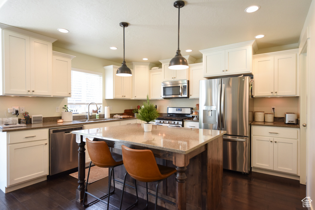 Kitchen with appliances with stainless steel finishes, dark wood-style flooring, a center island, white cabinetry, and recessed lighting