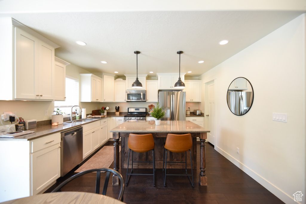 Kitchen featuring stainless steel appliances, dark wood-style flooring, a kitchen bar, a center island, and white cabinetry