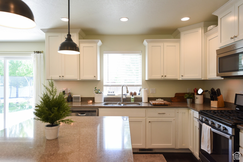 Kitchen featuring stainless steel appliances, white cabinets, recessed lighting, and hanging light fixtures