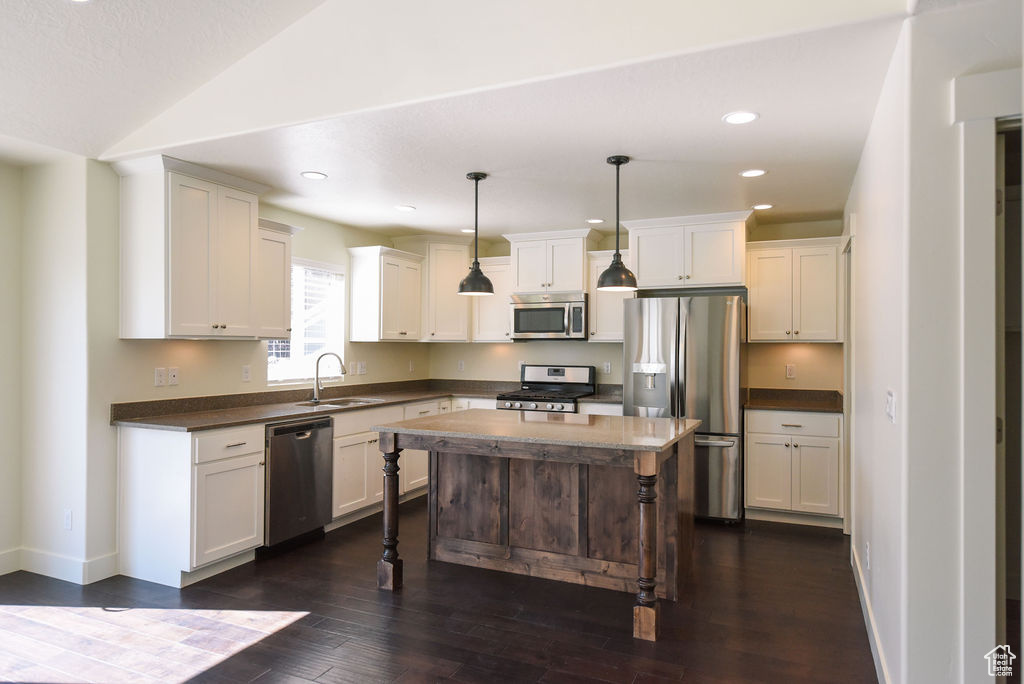 Kitchen featuring stainless steel appliances, dark countertops, dark wood finished floors, white cabinets, and a breakfast bar area