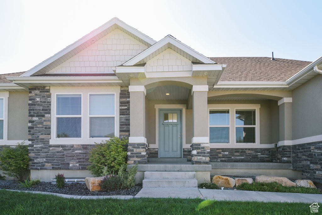 View of exterior entry featuring stone siding, stucco siding, and a shingled roof