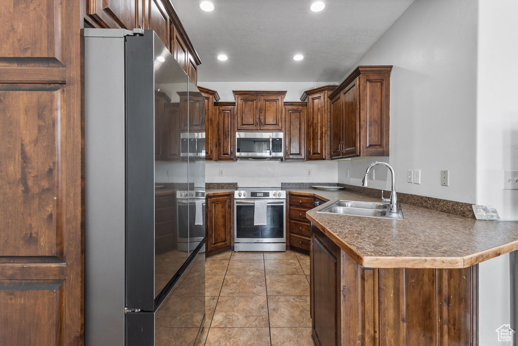 Kitchen with appliances with stainless steel finishes, a peninsula, recessed lighting, dark countertops, and light tile patterned floors