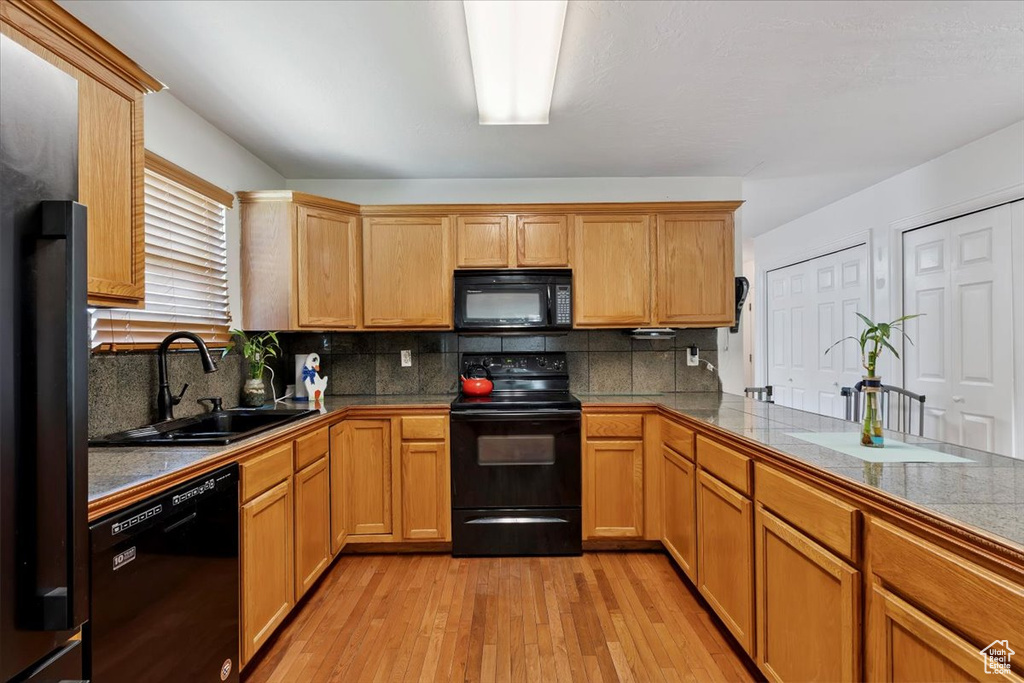 Kitchen with black appliances, light wood-style flooring, and tasteful backsplash